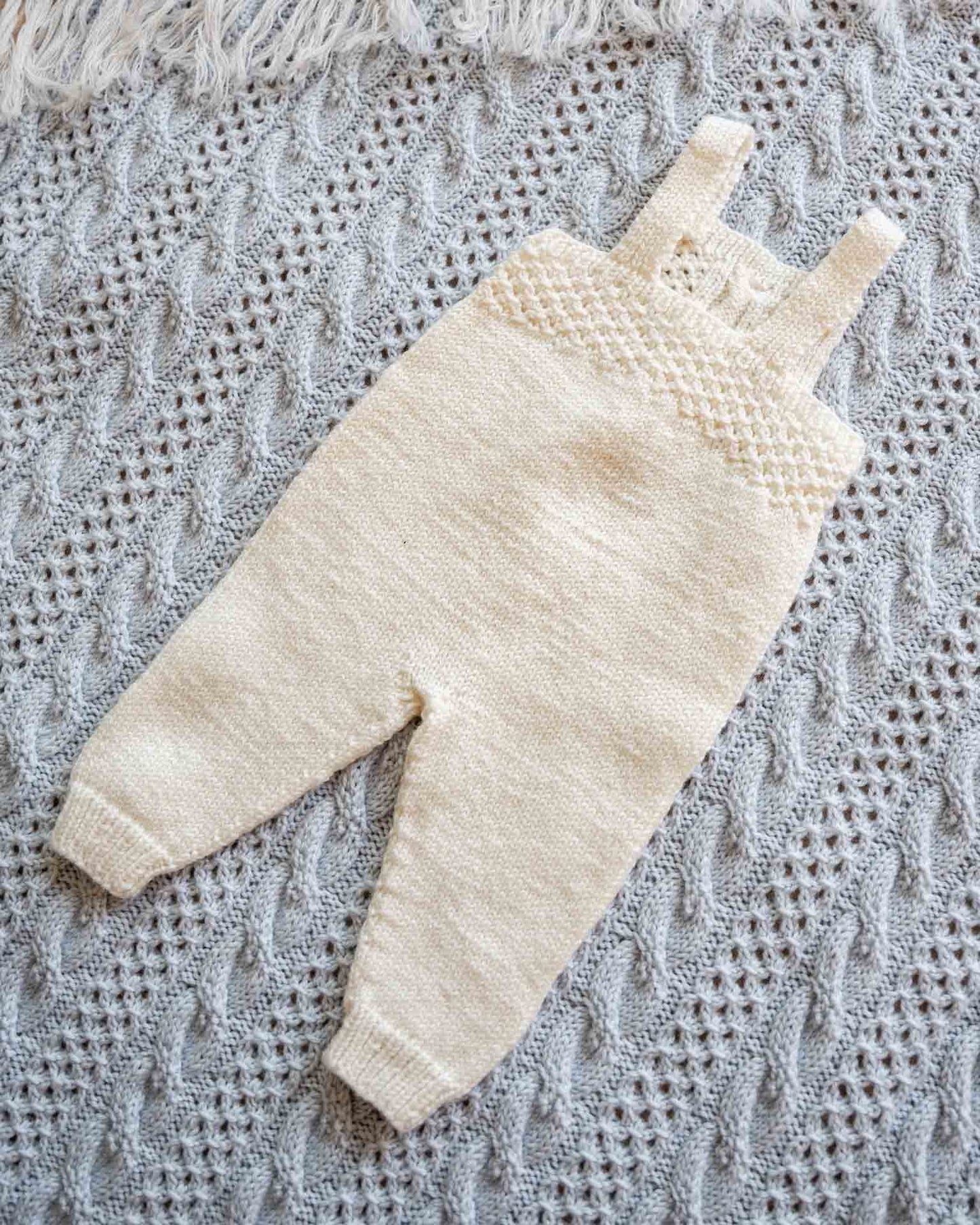 Selebuksen strikkes nedenfra og opp med strukturmønster på smekken og øverste del av bakstykket. Tidløs og klassisk selebukse for baby og barn. Baksiden av selebuksen.