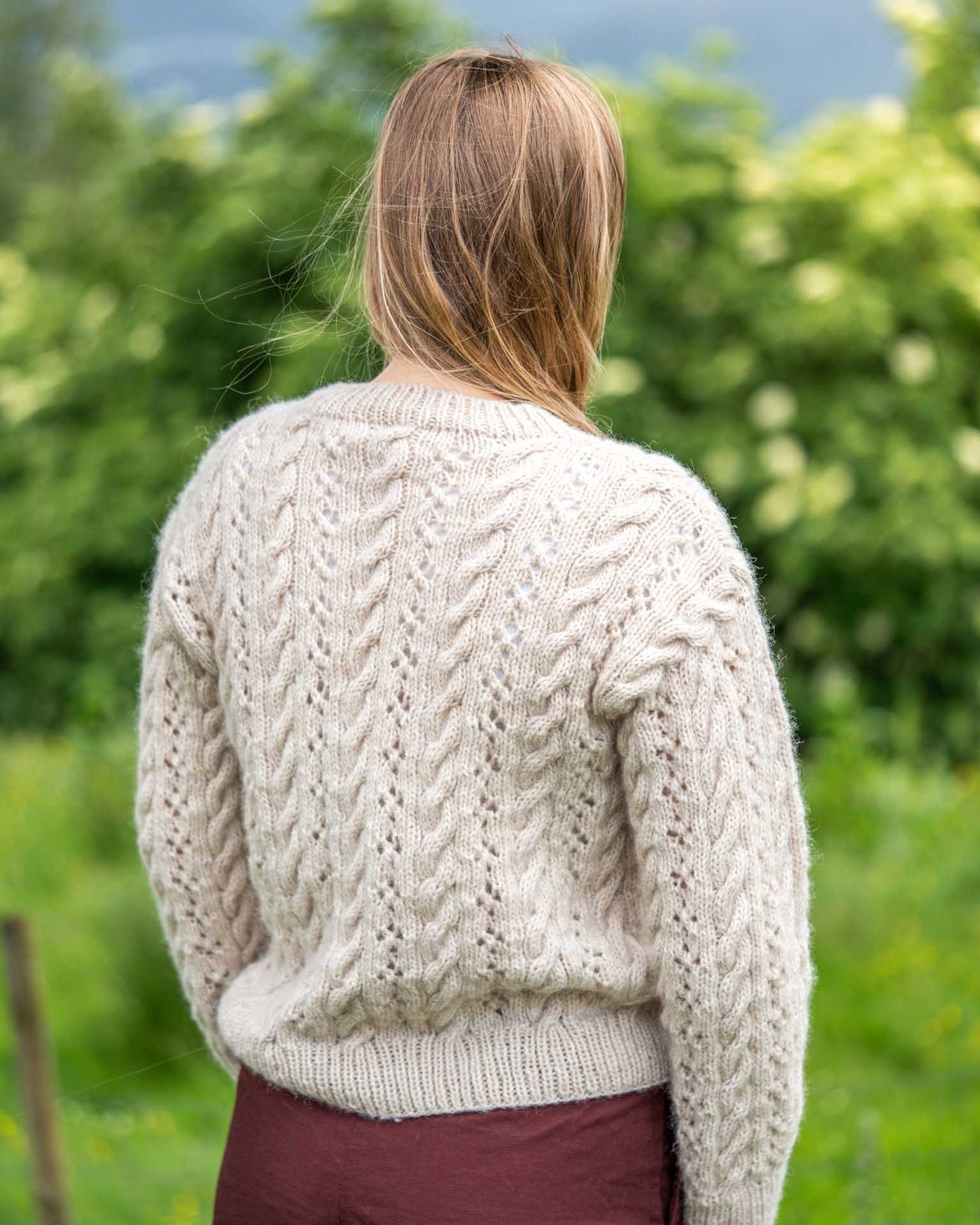 En lekker strukturstrikket genser med fletter og hullmønster. Like fin til jeans som over sommerkjolen. Genseren strikkes nedenfra og opp og det plukkes opp masker til ermene som strikkes ovenfra og ned. Baksiden av genseren.