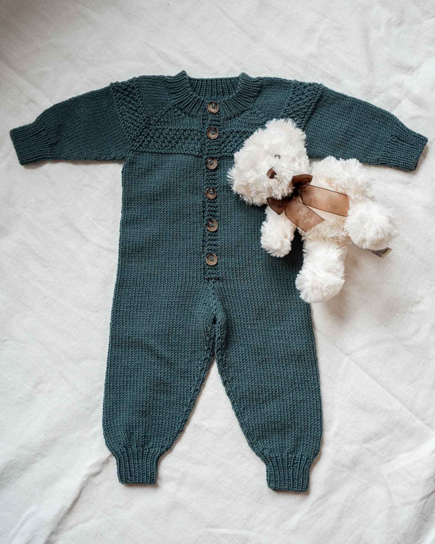 Hans babydress er en søt dress med perlestrikket bord på bærestykket. 
Dressen strikkes ovenfra og ned med raglanøkninger. 