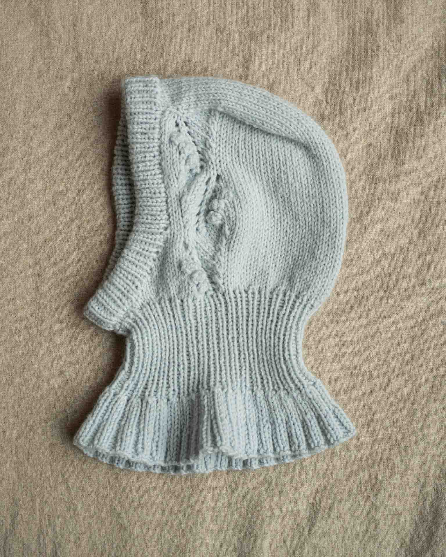 Helga Balaclava er en søt lue med nydelig struktur på begge sidene av luen. Balaklavaen strikkes ovenfra og ned. Kilen strikkes først før det plukkes opp masker langs sidene av denne. Videre strikkes det frem og tilbake med mønster før det økes til hals som strikkes rundt. Det økes deretter masker som danner en kappe rundt skuldre, rygg og bringe. Til slutt plukkes det opp masker og strikkes kant rundt ansiktsåpningen.