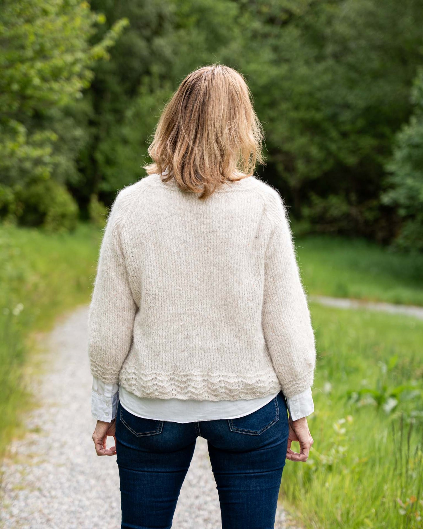 Karoline Bluse er en lett og luftig genser med trekvart ermer, den strikkes nedenfra og opp og kan strikkes kort eller lang. Blusen har blondekant på ermene, bolen og halsen. Bakside og rygg.