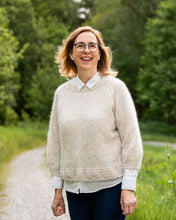 Last inn bildet i Galleri-visningsprogrammet, Karoline Bluse er en lett og luftig genser med trekvart ermer, den strikkes nedenfra og opp og kan strikkes kort eller lang. Blusen har blondekant på ermene, bolen og halsen. En nydelig pyntet og tidløs genser.
