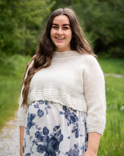 Karoline Bluse er en lett og luftig genser med trekvart ermer, den strikkes nedenfra og opp og kan strikkes kort eller lang. Blusen har blondekant på ermene, bolen og halsen.