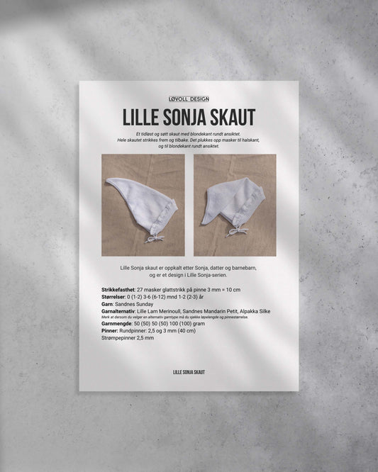 Et tidløst og søtt skaut med blondekant rundt ansiktet. Hele skautet strikkes frem og tilbake. Det plukkes opp masker til halskant, og til blondekant rundt ansiktet. Forside på strikkeoppskriften
