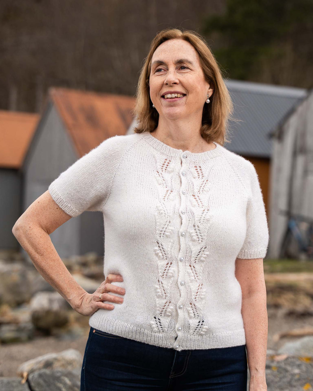 Helga Kortermet Cardigan er en lekker og stilren sommertopp med struktur på fremsiden. Den strikkes ovenfra og ned med to tråder, halsutringingen dannes ved vendepinner og stolpen strikkes i vrangbord samtidig som resten av arbeidet.