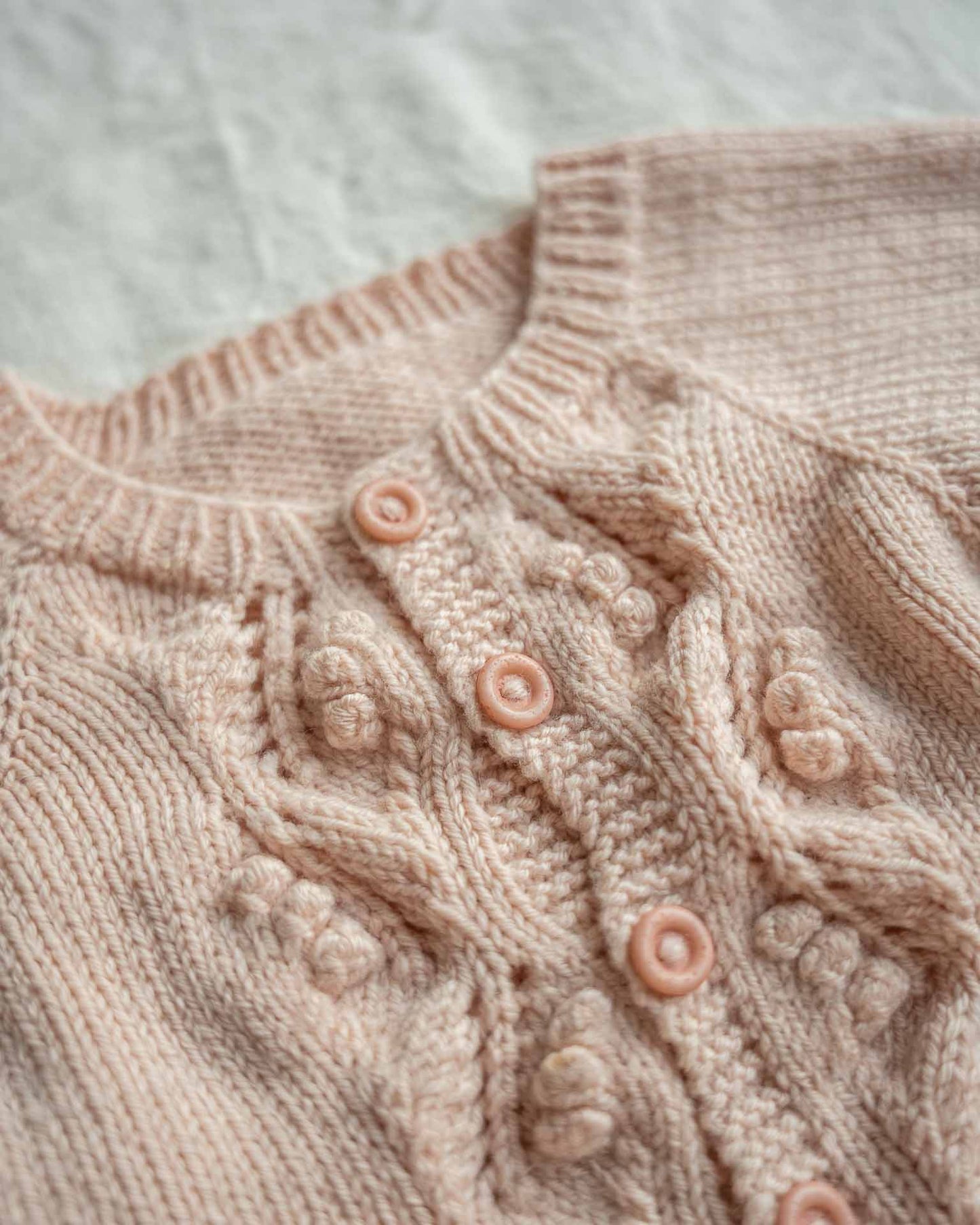 Helga babydress er en søt dress med struktur på fremsiden. Nærbilde av struktur og knapper.