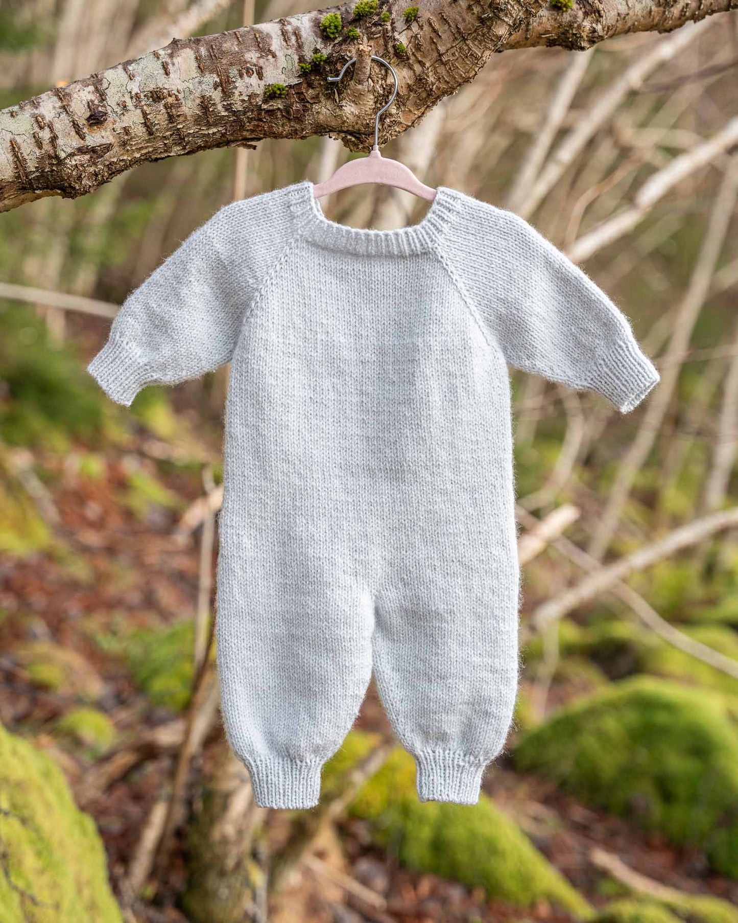 Helga babydress er en søt dress med struktur på fremsiden. Dressen strikkes ovenfra og ned, halsutringingen dannes ved vendepinner og stolpen strikkes i riller samtidig som resten av arbeidet. I en søt blåfarge. Baksiden.