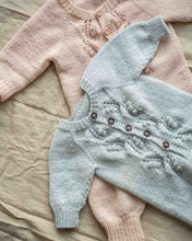 Last inn bildet i Galleri-visningsprogrammet, Helga babydress er en strikkedress med struktur på fremsiden. Strikkedressen strikkes ovenfra og ned, halsutringingen dannes ved vendepinner og stolpen strikkes i riller samtidig som resten av arbeidet. 
